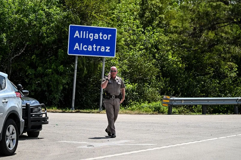 Florida State Trooper in front of an 'Alligator Alcatraz" sign