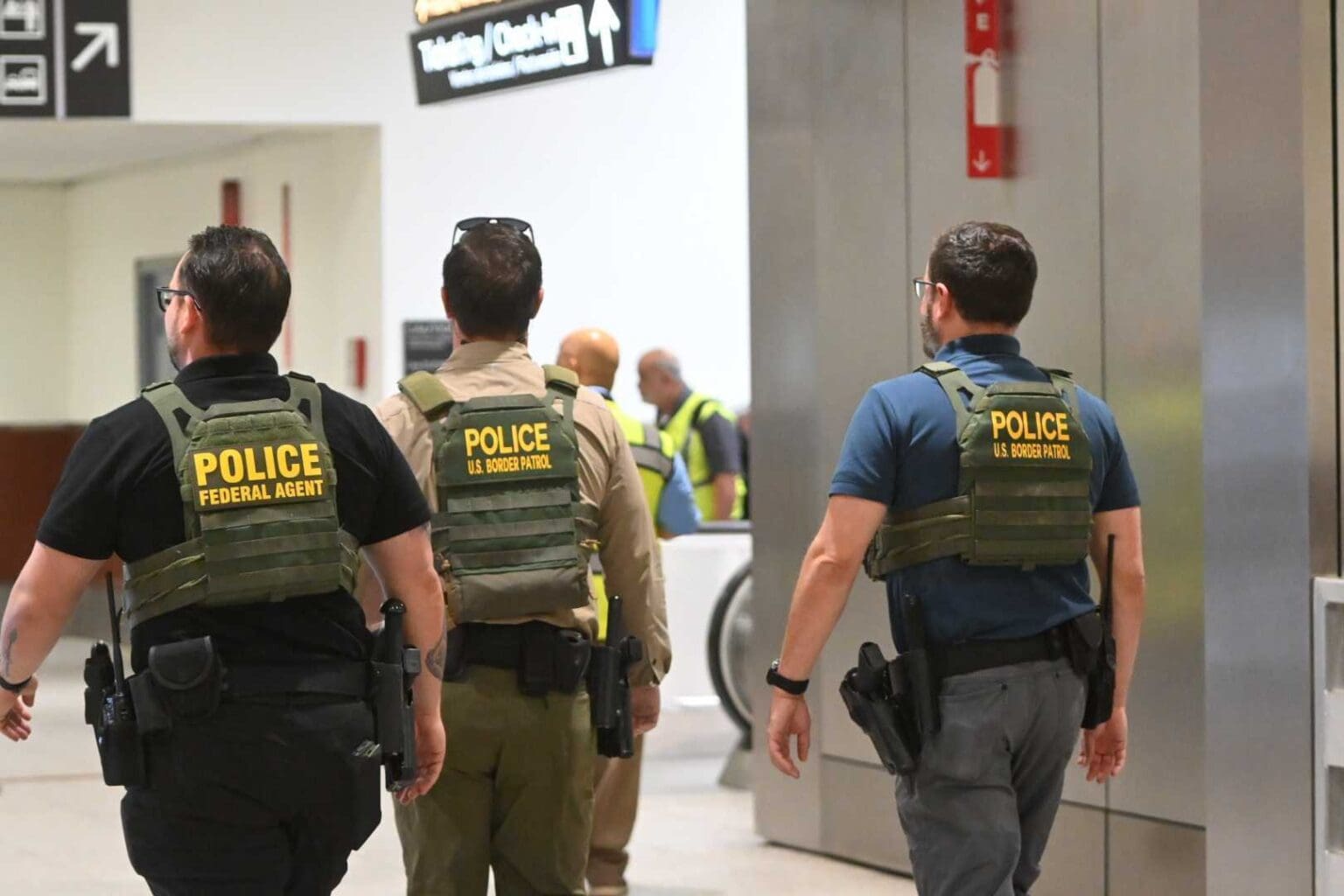 Three armed federal officers in bulletproof vests in a hallway.